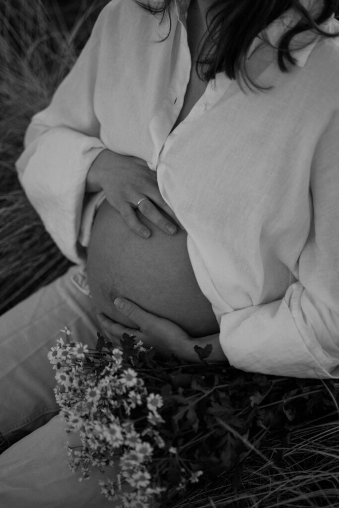 utsnitt av en gravid kvinne som holder rundt magen sin med en blomsterbukett på fanget